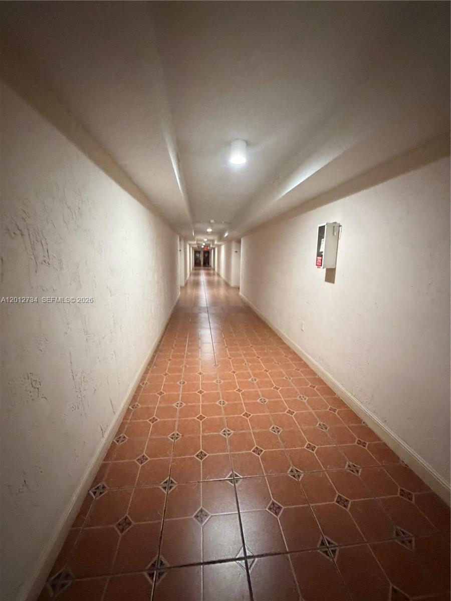 A long, narrow hallway features terracotta-colored floor tiles and plain white walls — 1300 SW 122nd Ave # 2, Miami FL 33184, MIAMI, FL