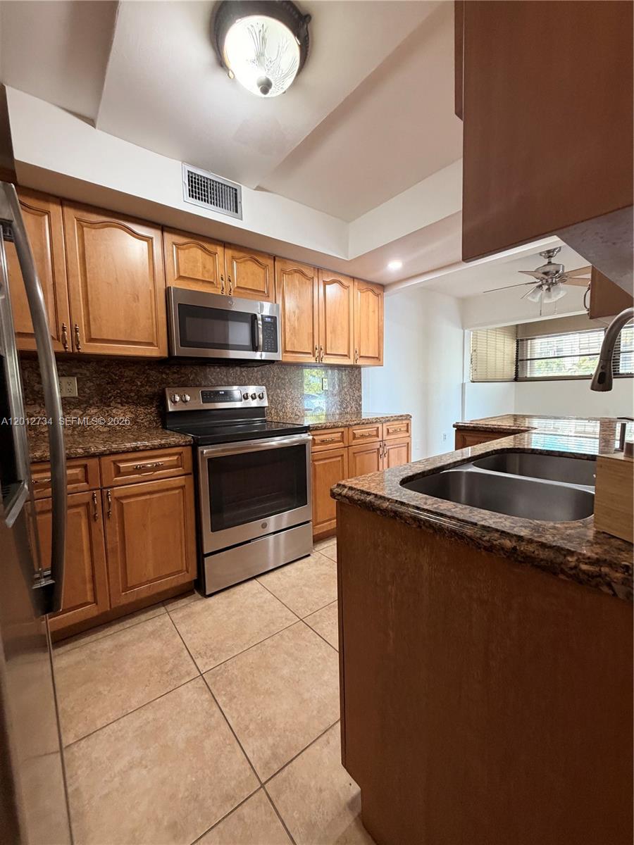 A kitchen features wood cabinets, granite countertops, stainless steel appliances, and beige tile flooring — 1300 SW 122nd Ave # 2, Miami FL 33184, MIAMI, FL