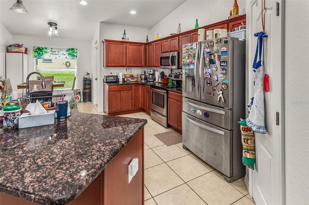 A kitchen features dark wood cabinets, granite countertops, stainless steel appliances, and tile flooring — 215 CAPTAIN HOOK WAY, DAVENPORT, FL