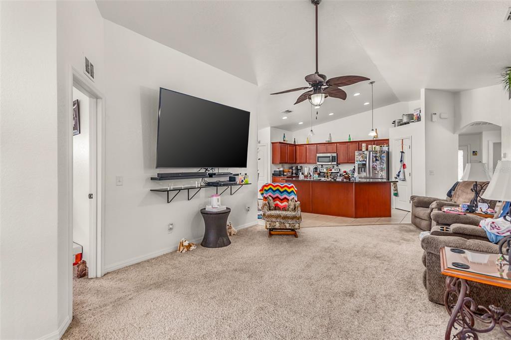 A living room with carpeted floors, a wall-mounted television, and an open kitchen beyond — 215 CAPTAIN HOOK WAY, DAVENPORT, FL