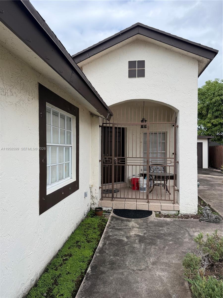 A white stucco house features a gated front porch and a dark-trimmed window — 14249 SW 103rd Ter, Miami FL 33186, MIAMI, FL