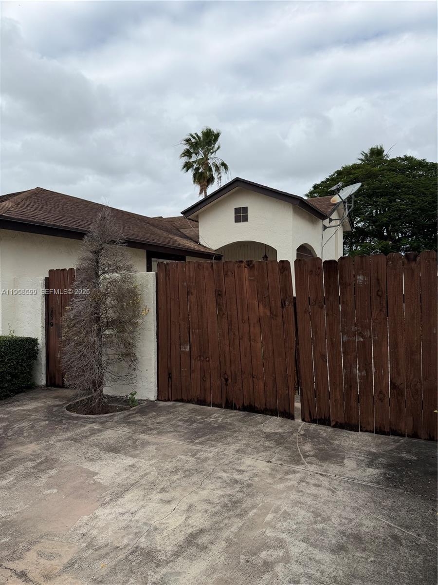 A wooden fence stands in front of a stucco house with a brown roof — 14249 SW 103rd Ter, Miami FL 33186, MIAMI, FL