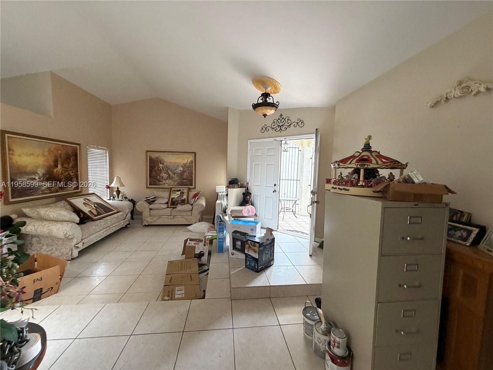 A living room with tiled floors, vaulted ceilings, and an open door leading outside — 14249 SW 103rd Ter, Miami FL 33186, MIAMI, FL
