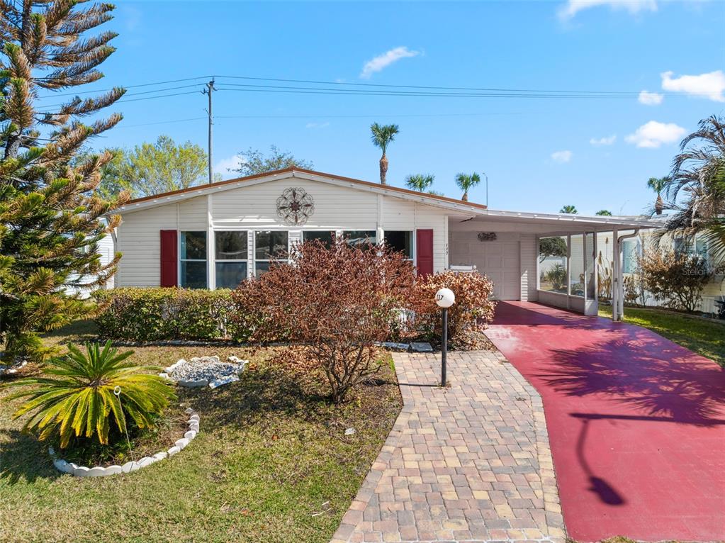 A single-story house features light siding, red shutters, a paved walkway, and a red driveway — 117 WOODSMILL BOULEVARD UNIT 45, COCOA, FL