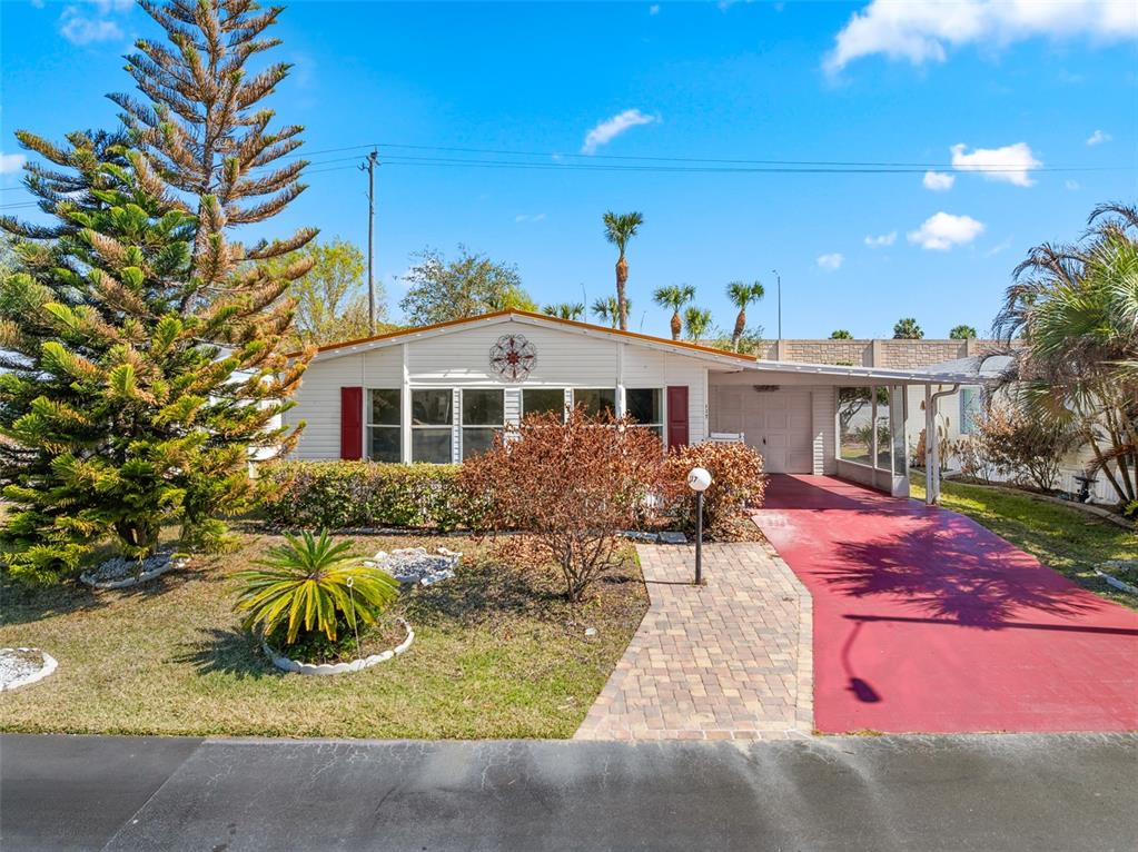 A single-story mobile home features a red driveway, a brick walkway, and a large pine tree — 117 WOODSMILL BOULEVARD UNIT 45, COCOA, FL
