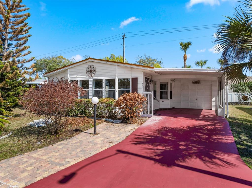 A single-story mobile home features a red driveway, a paved walkway, and a carport — 117 WOODSMILL BOULEVARD UNIT 45, COCOA, FL