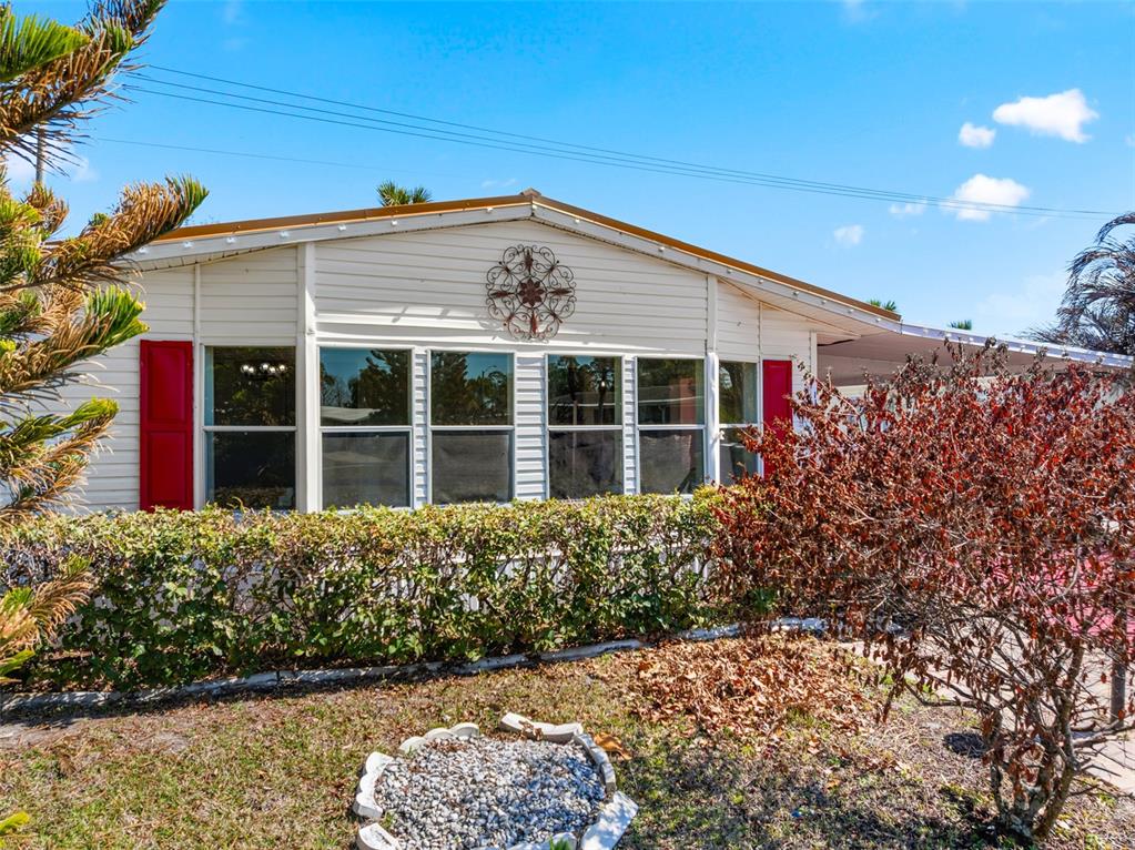The exterior of a single-story manufactured home features white siding, red shutters, and landscaping — 117 WOODSMILL BOULEVARD UNIT 45, COCOA, FL