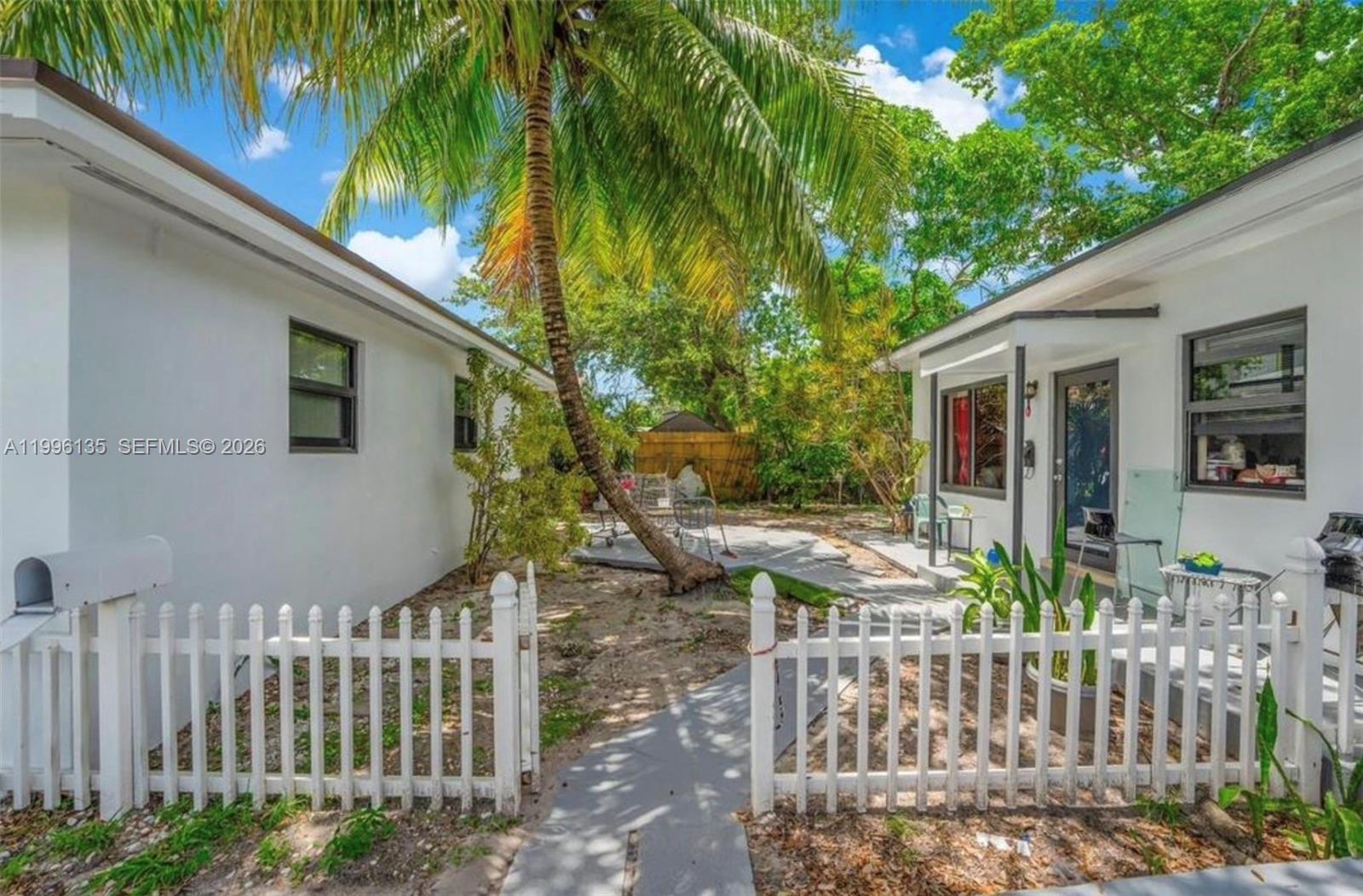 A white picket fence encloses a courtyard between two white buildings with a palm tree — 7625 NW 4th Ct, Miami FL 33150, MIAMI, FL