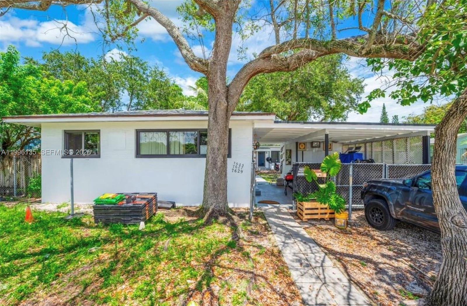 A single-story white house features a carport, a large tree in the front yard, and fencing — 7625 NW 4th Ct, Miami FL 33150, MIAMI, FL