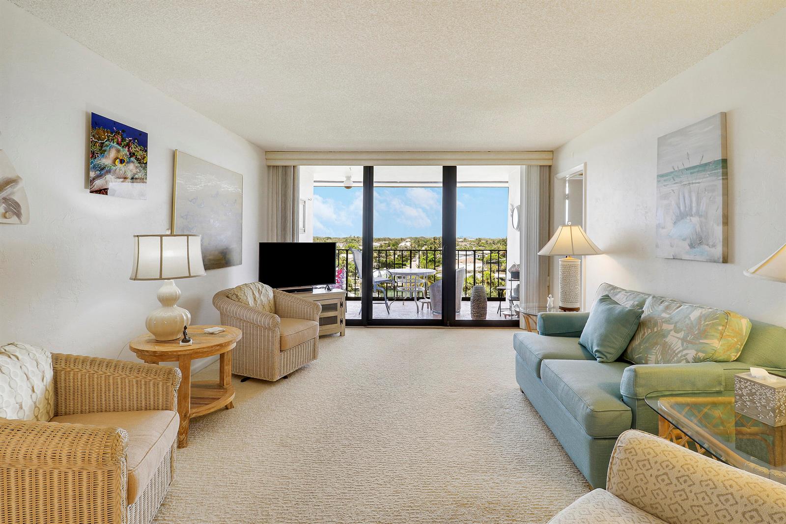 A living room features wicker chairs, a blue sofa, and a balcony with an outdoor view — 225 S Beach Road # 605, Jupiter FL 33469, JUPITER, FL