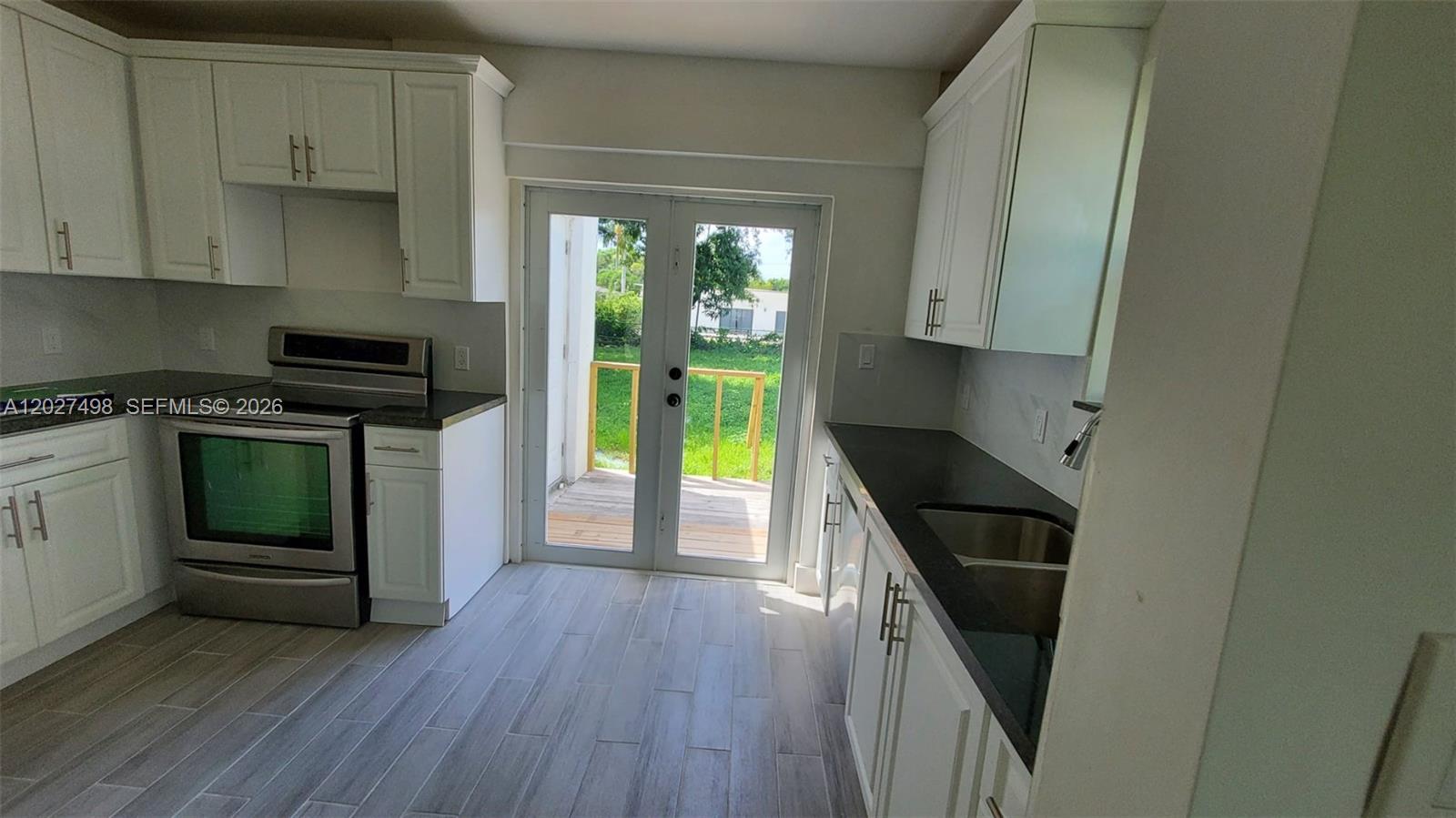 A kitchen features white cabinets, black countertops, stainless steel appliances, and a glass door — 560 NW 53rd St, Miami FL 33127, MIAMI, FL