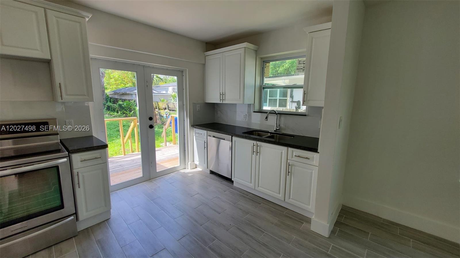A kitchen features white cabinets, dark countertops, stainless steel appliances, and a glass door — 560 NW 53rd St, Miami FL 33127, MIAMI, FL