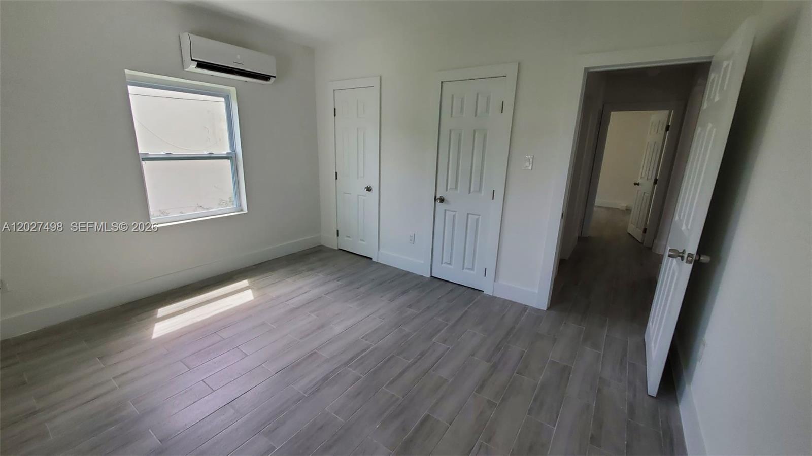 A bedroom with gray wood-look tile flooring, white walls, two closet doors, and a window — 560 NW 53rd St, Miami FL 33127, MIAMI, FL