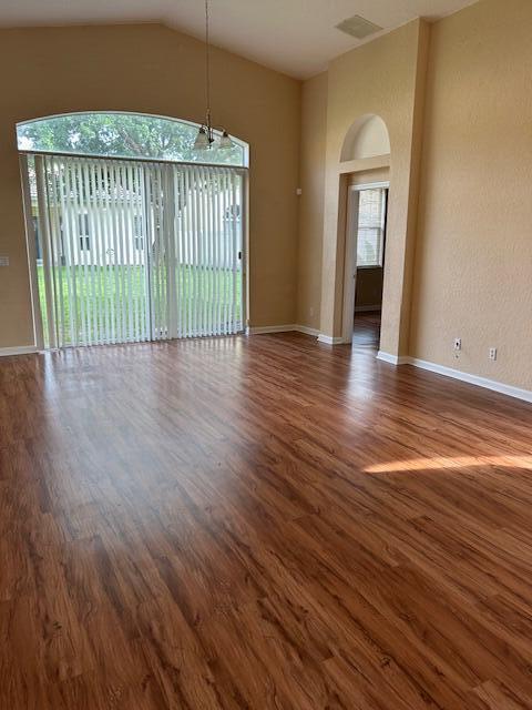 An empty room features wood-look flooring, a vaulted ceiling, and a large sliding glass door — 5642 Sunberry Circle, Fort Pierce FL 34951, FORT PIERCE, FL