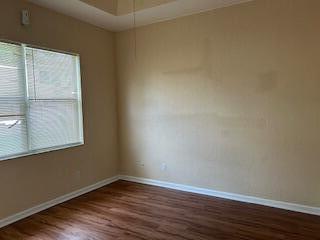 An empty room features wood-look flooring, beige walls, and a window with white blinds — 5642 Sunberry Circle, Fort Pierce FL 34951, FORT PIERCE, FL