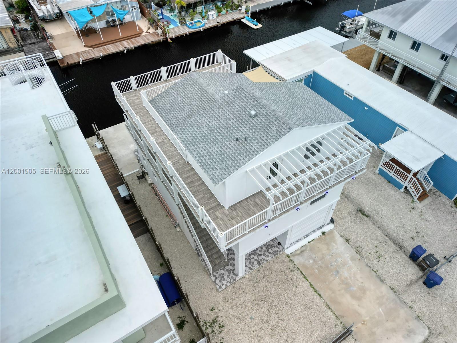 An elevated white house with a large deck and pergola sits beside a canal — 20 Eagle Dr, Key Largo FL 33037, KEY LARGO, FL