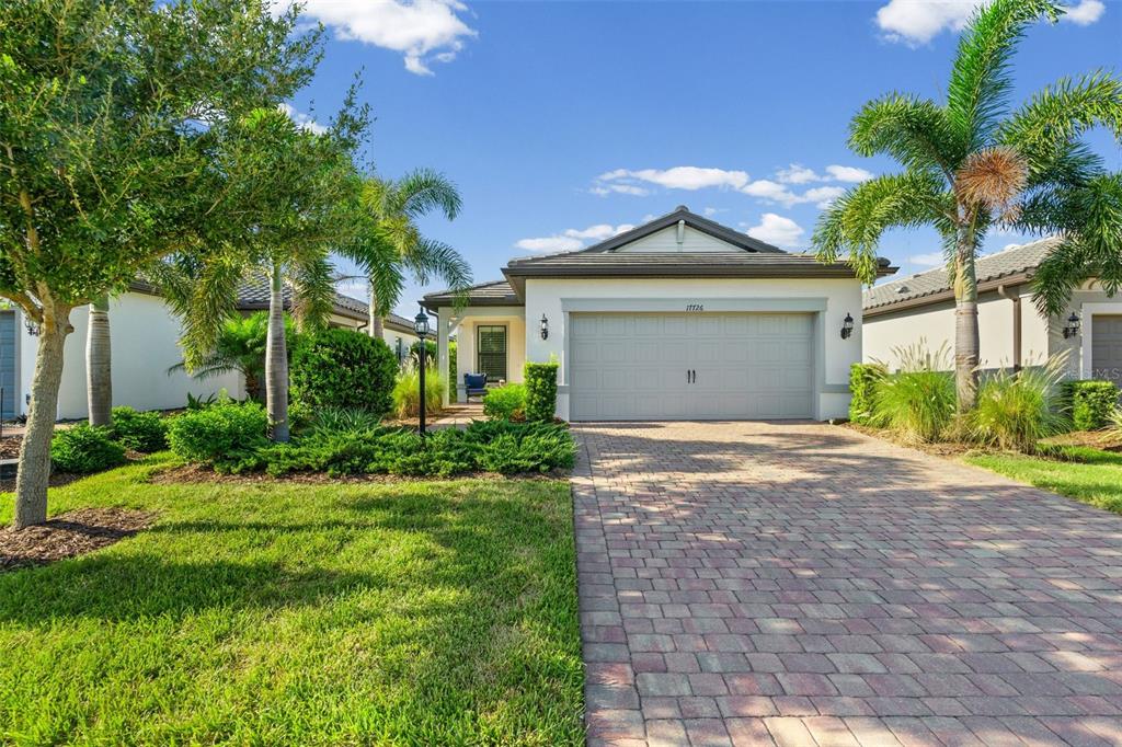 A single-story house with a paved driveway, a two-car garage, and surrounding palm trees — 17726 NORTHWOOD PLACE, BRADENTON, FL