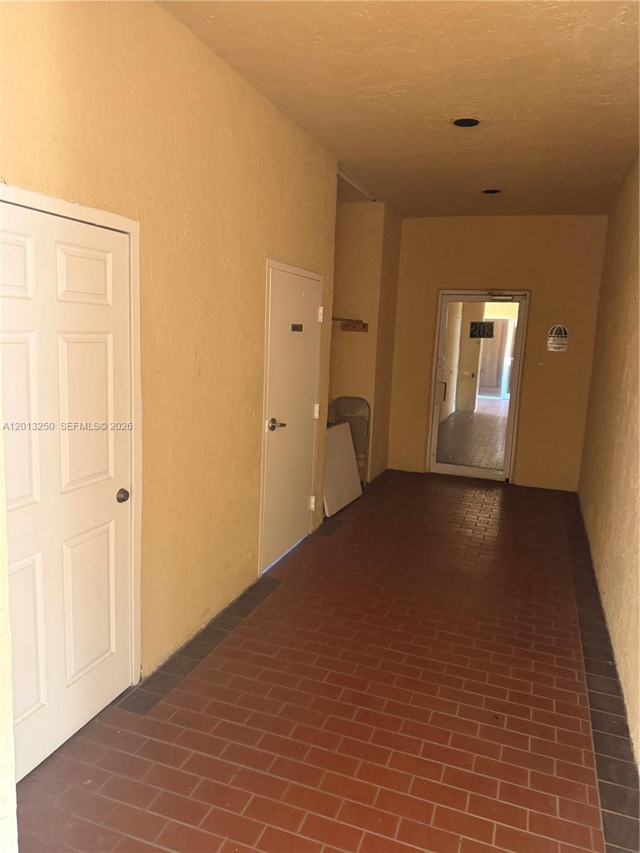A hallway with a brick floor leads to a glass door marked 203 — 7400 NW 7th St # 201, Miami FL 33126, MIAMI, FL