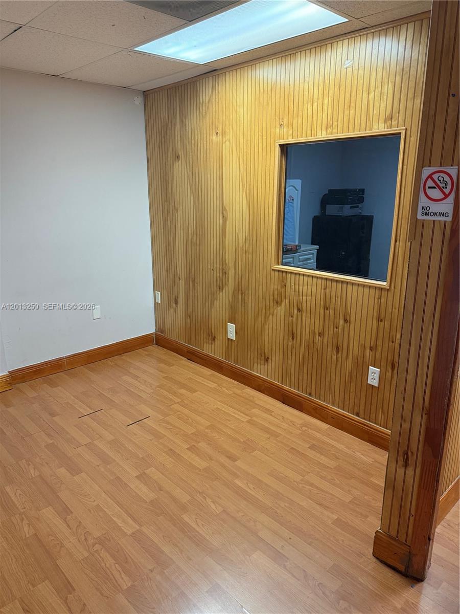 An office room features wood-paneled walls, wood-look flooring, and a rectangular interior window — 7400 NW 7th St # 201, Miami FL 33126, MIAMI, FL
