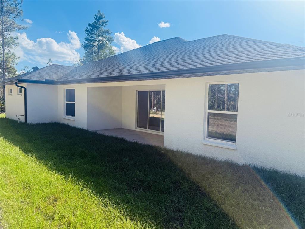 The exterior of a white stucco house features a covered patio and sliding glass doors — 13465 CANYON SWALLOW ROAD, WEEKI WACHEE, FL