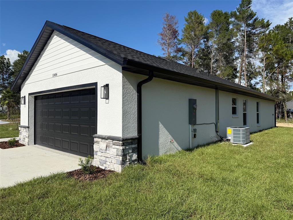 A white stucco garage with a black roof, stone accents, and a dark garage door — 13465 CANYON SWALLOW ROAD, WEEKI WACHEE, FL