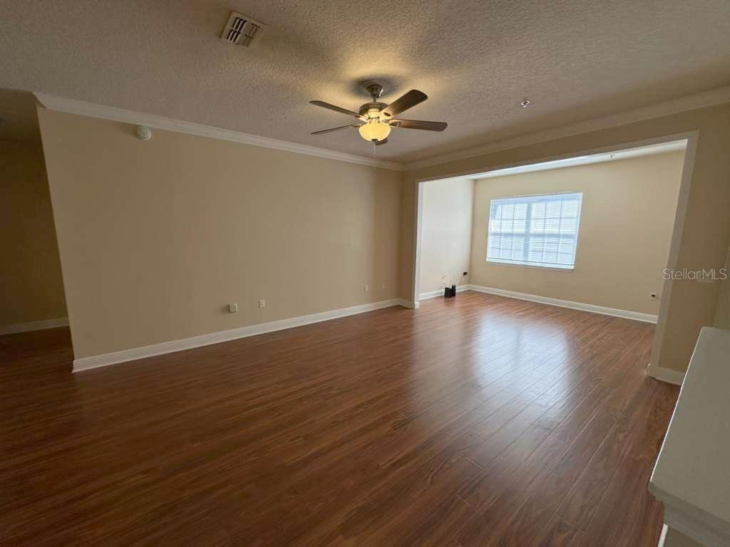 A living room with wood-look flooring, a ceiling fan, and a recessed window area — 225 SOUTHERN PECAN CIRCLE UNIT 208, WINTER GARDEN, FL