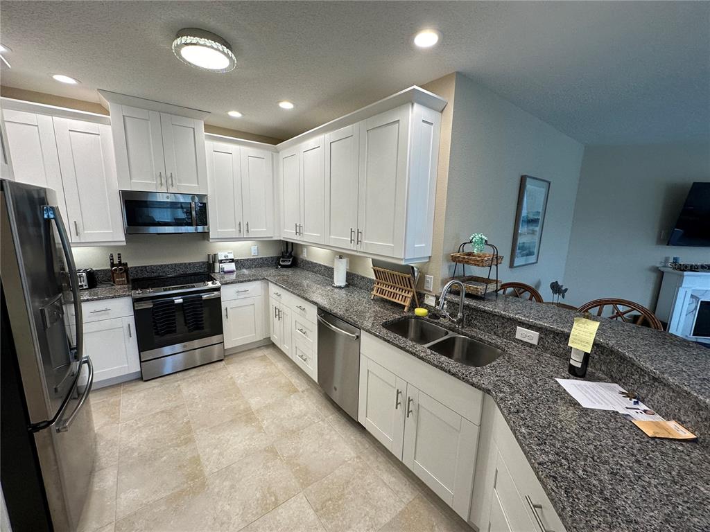A kitchen features white cabinets, granite countertops, stainless steel appliances, and light-colored tile flooring — 3412 79TH STREET CIRCLE W UNIT 103, BRADENTON, FL