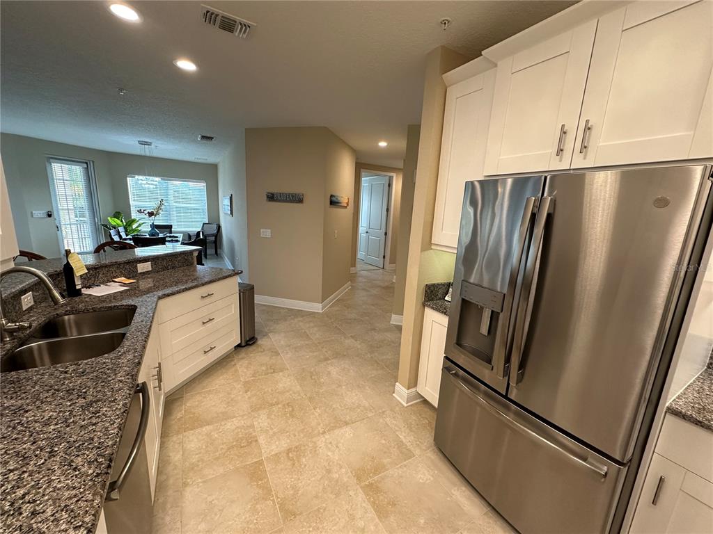 A kitchen with granite countertops, white cabinets, and stainless steel appliances opens to a dining area — 3412 79TH STREET CIRCLE W UNIT 103, BRADENTON, FL