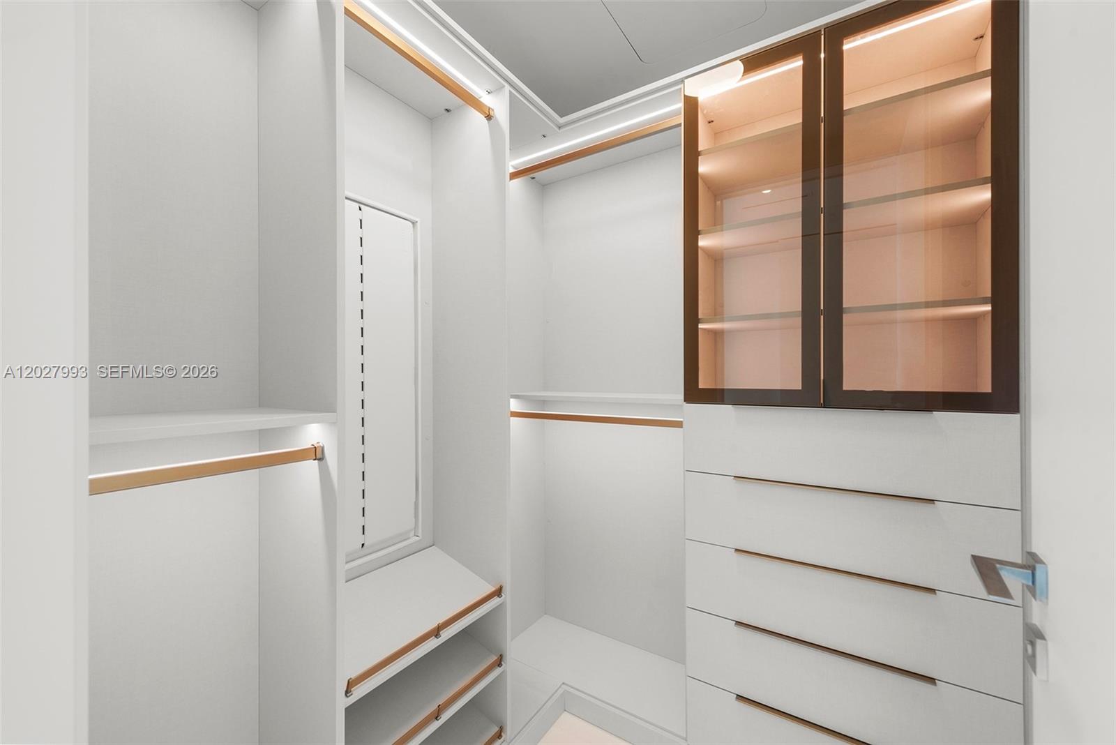 A modern walk-in closet features white cabinetry, gold-toned hardware, and integrated LED shelf lighting — 300 Biscayne Boulevard Way # 3905W, Miami FL 33131, MIAMI, FL