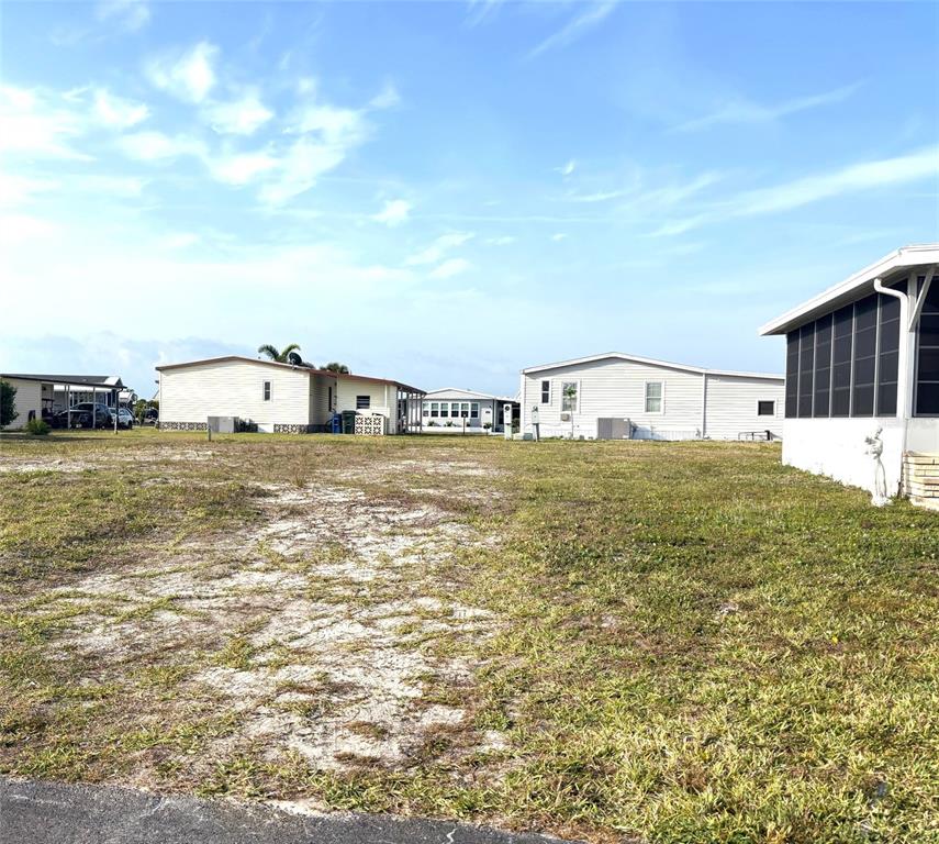 A vacant grassy lot sits between several manufactured homes under a bright blue sky — 647 LOS ALTOS, NORTH PORT, FL