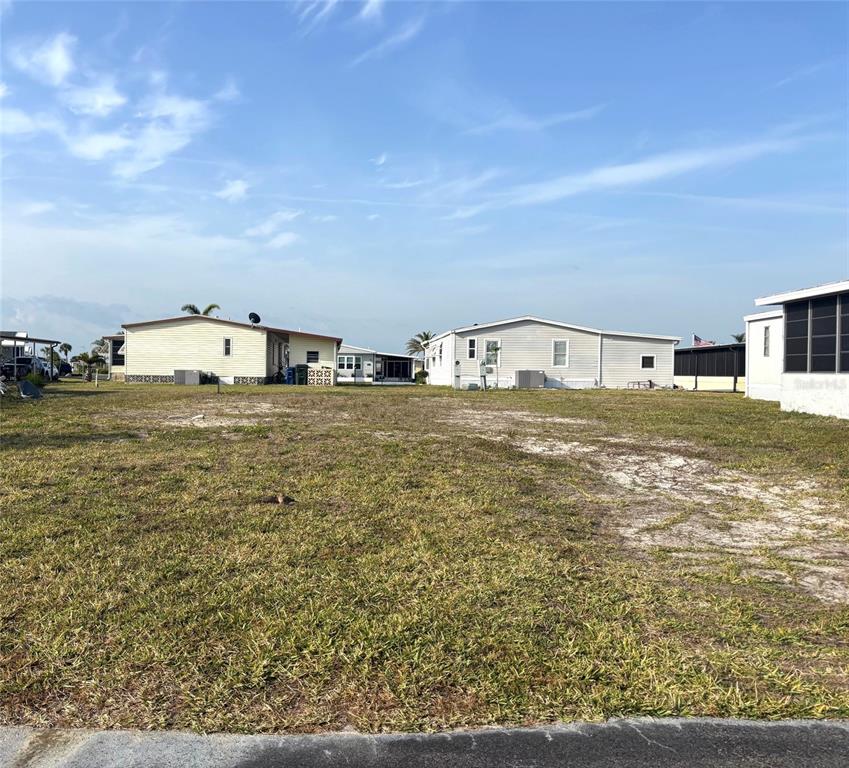 A vacant, grassy lot sits between several manufactured homes under a clear blue sky — 647 LOS ALTOS, NORTH PORT, FL