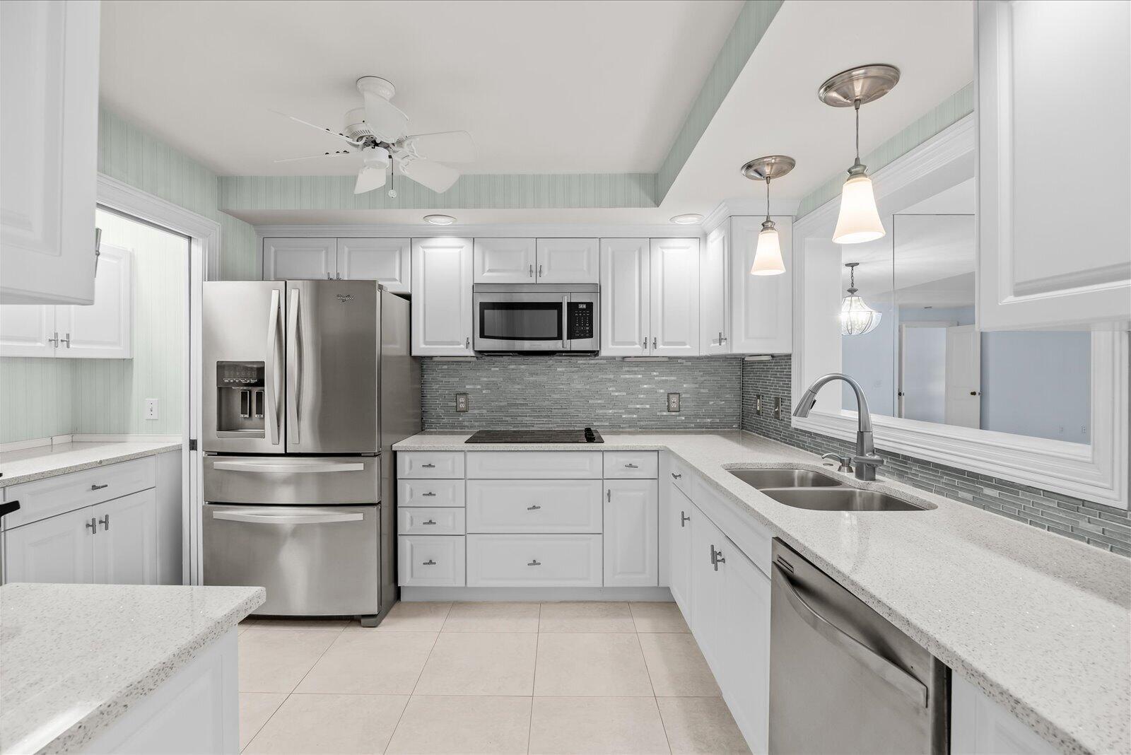 A kitchen with white cabinets, stainless steel appliances, a gray tile backsplash, and quartz countertops — 1903 Bay Road # 206, Vero Beach FL 32963, VERO BEACH, FL