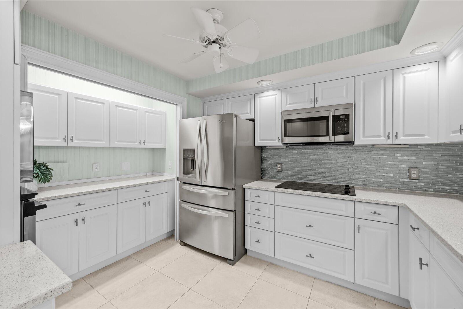 A kitchen features white cabinetry, stainless steel appliances, a gray tiled backsplash, and light countertops — 1903 Bay Road # 206, Vero Beach FL 32963, VERO BEACH, FL