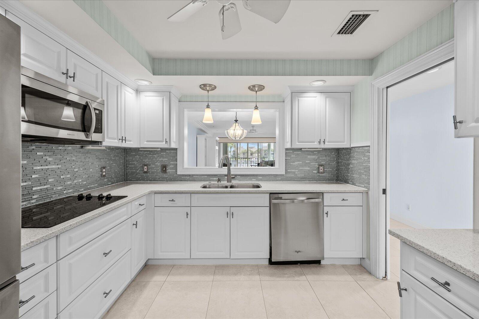 A white kitchen features stainless steel appliances, a gray tiled backsplash, and a pass-through window — 1903 Bay Road # 206, Vero Beach FL 32963, VERO BEACH, FL