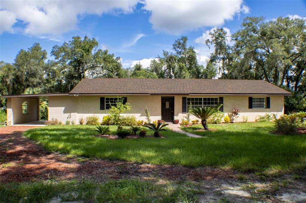 A single-story ranch-style house with a carport, tan stucco exterior, and a dark shingled roof — 111 HIGHLAND STREET, ORANGE CITY, FL