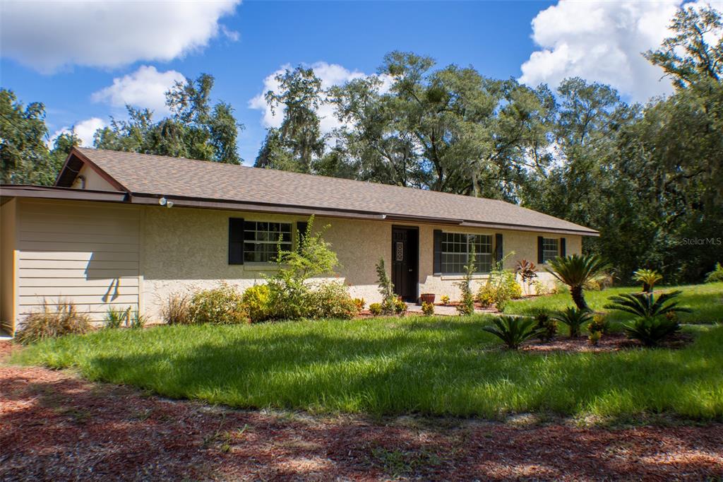 A single-story house with a tan stucco exterior, dark shutters, and a brown shingled roof — 111 HIGHLAND STREET, ORANGE CITY, FL