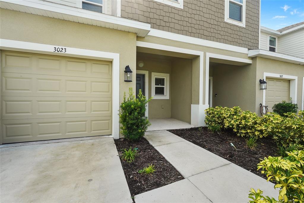 A tan townhouse exterior features a single-car garage, a covered entryway, and landscaped garden beds — 3023 NOVARA LANE, BRADENTON, FL