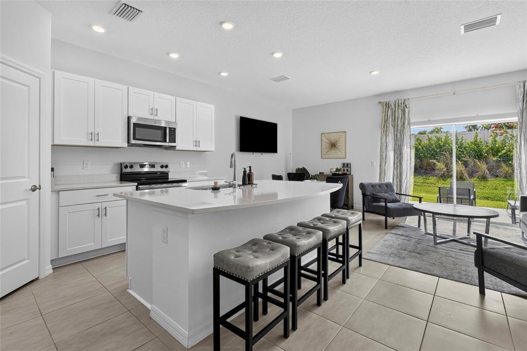 A modern kitchen features white cabinets, a large island with bar seating, and tile flooring — 3023 NOVARA LANE, BRADENTON, FL