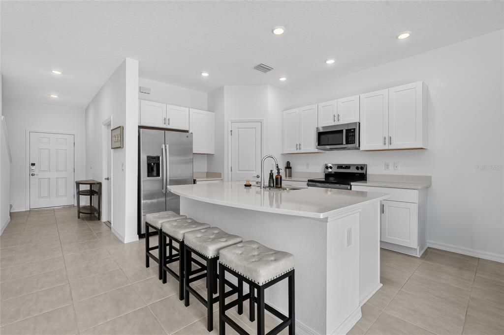A modern kitchen features white cabinets, stainless steel appliances, and a large island with seating — 3023 NOVARA LANE, BRADENTON, FL