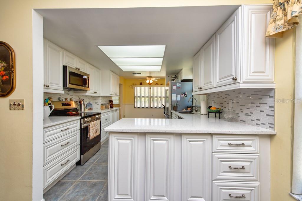 A kitchen features white cabinets, quartz countertops, a tiled backsplash, and stainless steel appliances — 1605 LELAND DRIVE, SUN CITY CENTER, FL