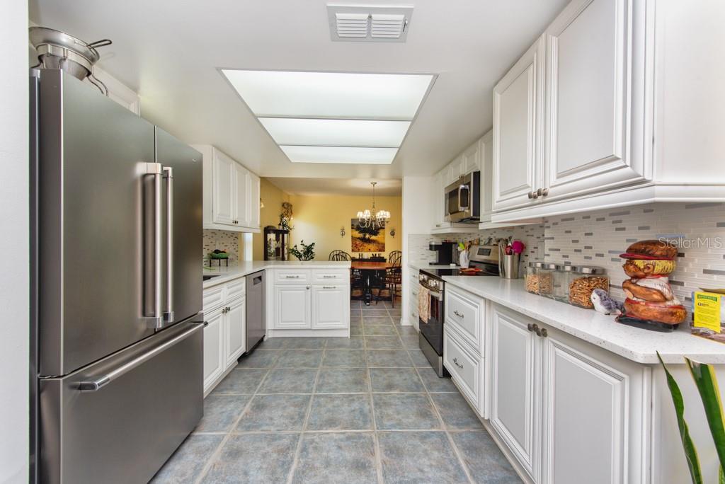 A galley kitchen features white cabinets, stainless steel appliances, quartz countertops, and blue tile flooring — 1605 LELAND DRIVE, SUN CITY CENTER, FL