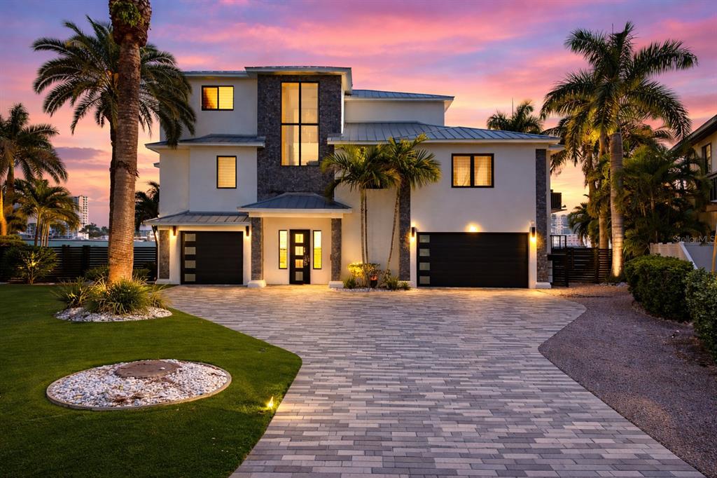A modern two-story house with a stone facade, two garages, and a paved driveway at sunset — 7801 9TH AVENUE S, ST PETERSBURG, FL