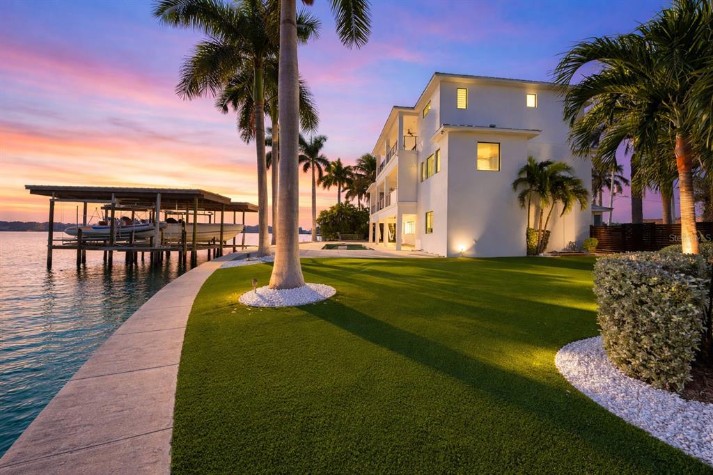 A multi-story white house sits on a grassy lawn beside a boat dock at sunset — 7801 9TH AVENUE S, ST PETERSBURG, FL