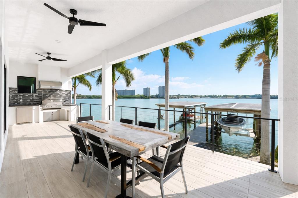 A covered outdoor patio features a dining table, an integrated grill, and waterfront views — 7801 9TH AVENUE S, ST PETERSBURG, FL