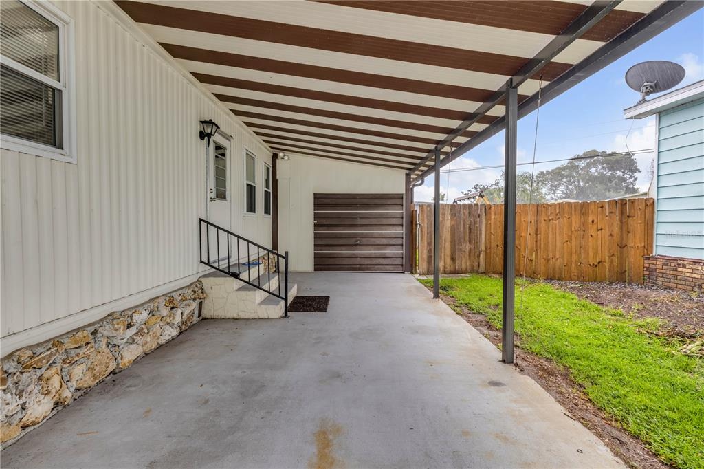 A covered concrete carport sits beside a mobile home with stone skirting and wooden fencing — 130 PINE STREET, EDGEWATER, FL