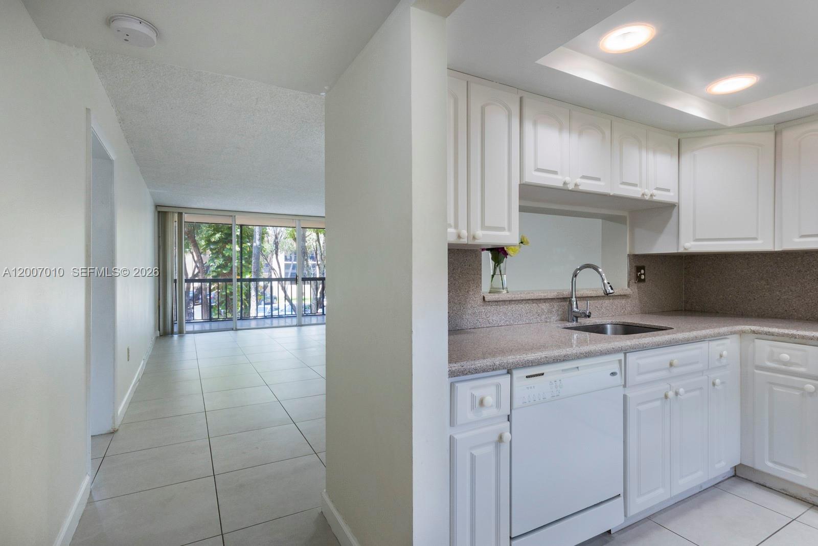 A white kitchen with granite countertops overlooks a tiled living area with a balcony — 10855 SW 112th Ave # 211, Miami FL 33176, MIAMI, FL