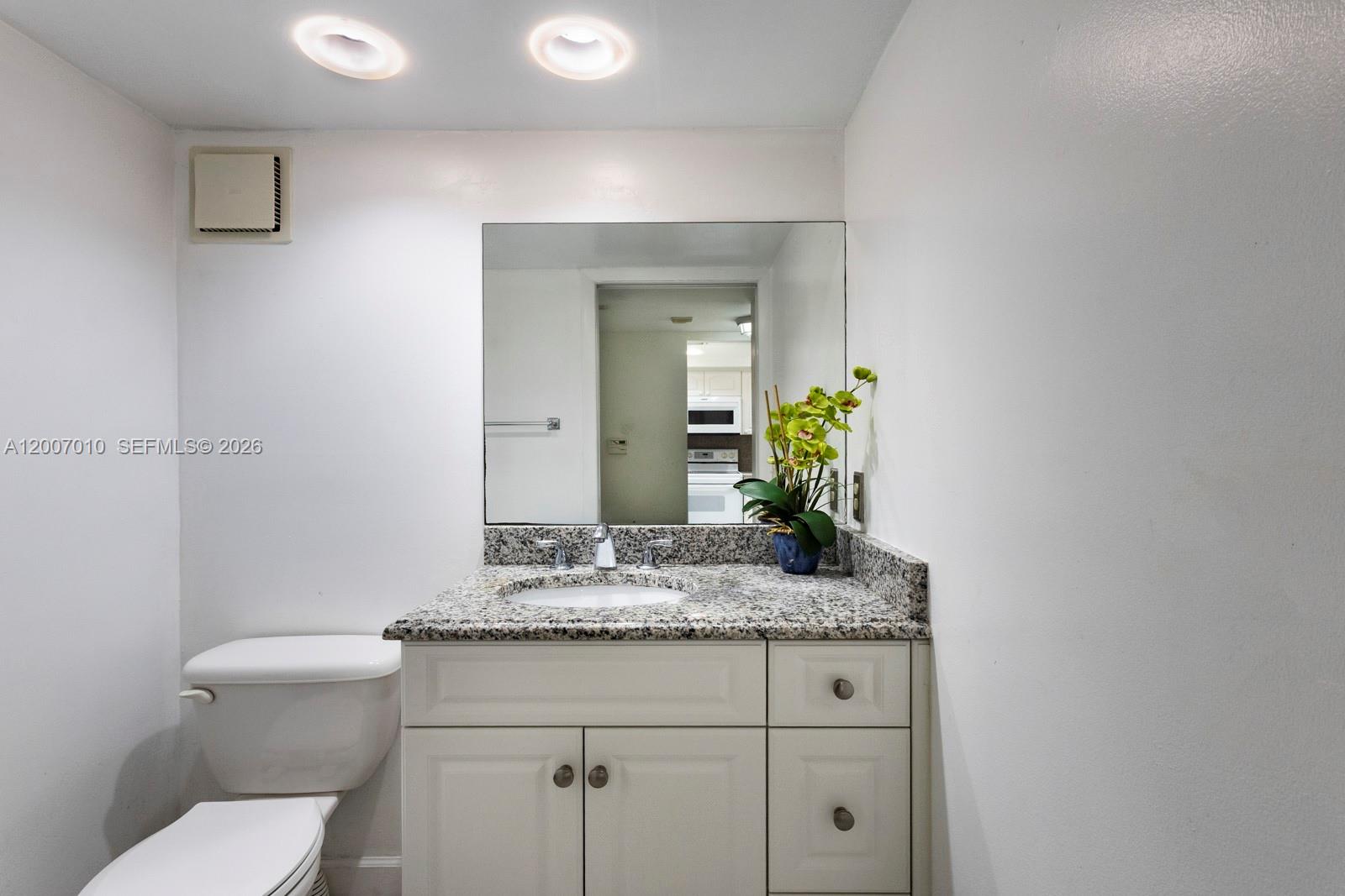 A bathroom features a granite vanity countertop, white cabinets, a toilet, and a wall mirror — 10855 SW 112th Ave # 211, Miami FL 33176, MIAMI, FL