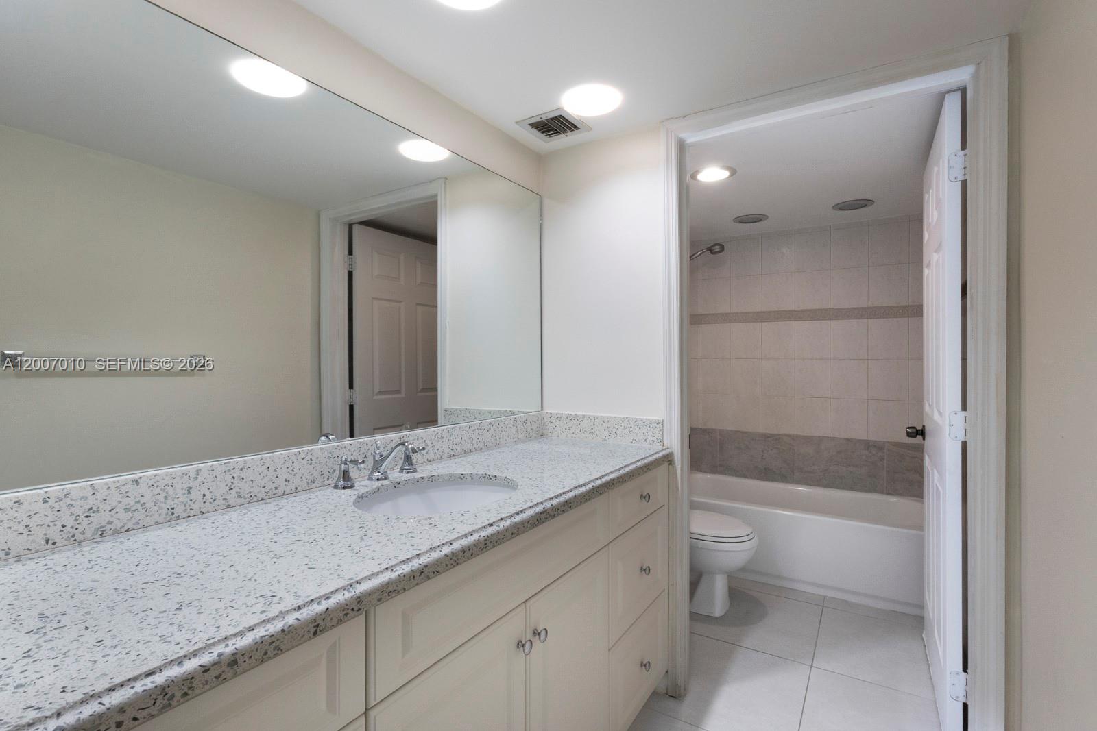 A bathroom features a speckled granite vanity countertop, white cabinetry, and an adjacent tiled tub-shower — 10855 SW 112th Ave # 211, Miami FL 33176, MIAMI, FL