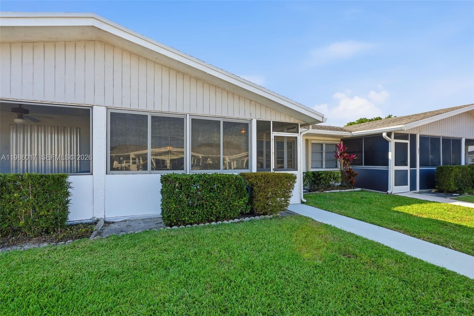 The exterior of a single-story home features a screened-in porch and a manicured lawn — 3471 Christopher St, West Palm Beach FL 33417, WEST PALM BEACH, FL