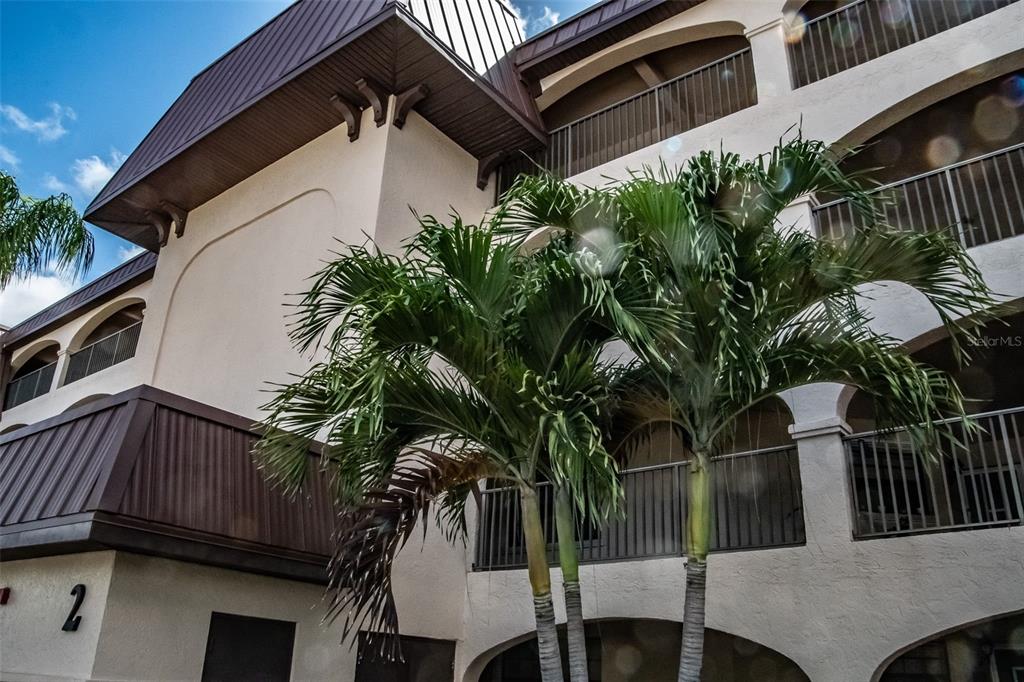 A low-angle view of a multi-story building exterior with balconies and palm trees — 23465 HARBORVIEW ROAD UNIT 245, PUNTA GORDA, FL